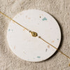Gold bracelet with a gold charm and pearl beads on a round, speckled coaster 