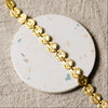 Gold disc bracelet on a white round, speckled coaster surface