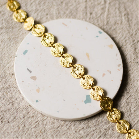 Gold disc bracelet on a white round, speckled coaster surface