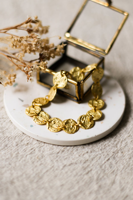 Gold bracelet on a white speckled coaster with a glass jewellery box and dried flowers in the background