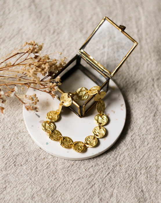 Gold bracelet on a white speckled coaster with a glass jewellery box and dried flowers in the background
