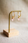 Gold hoop earrings with rose quartz stones on a brass stand with a neutral background