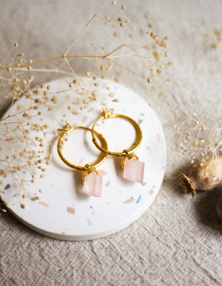 Gold hoop earrings with rose quartz stones on a round white dish with dried flowers.