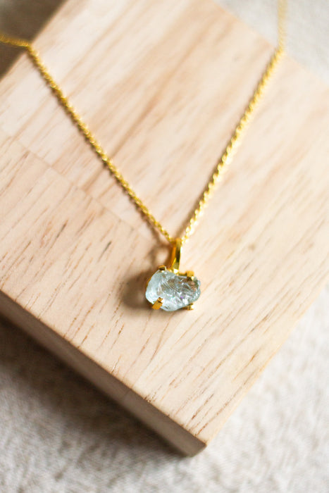 Gold necklace with an aqua pendant on a wooden block