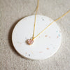 Gold necklace with a morganite pendant on a white terrazzo and linen surface
