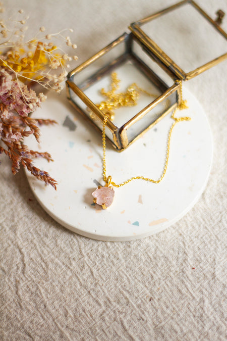 Gold necklace with a morganite pendant on a linen surface with dried flowers.