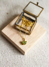 Gold necklace with a prenite pendant in an open glass and brass jewellery box on a wooden block.