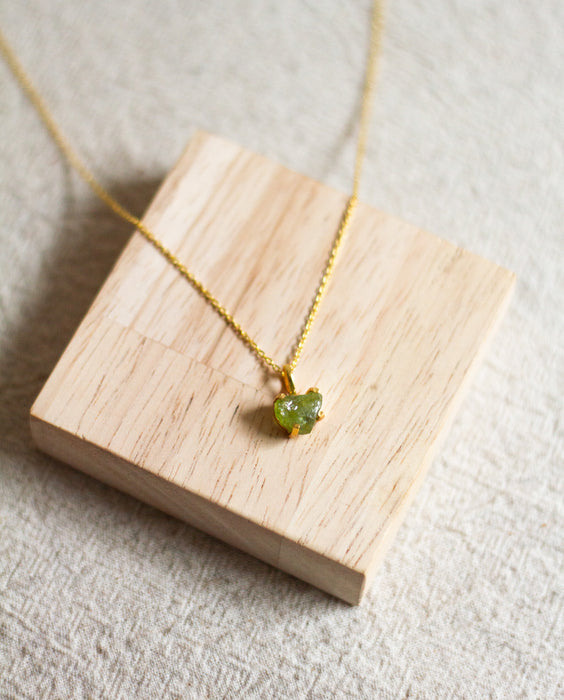 Gold necklace with a prenite pendant on a wooden block and a linen surface