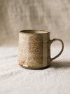 Speckled ceramic mug on a textured surface with a neutral background