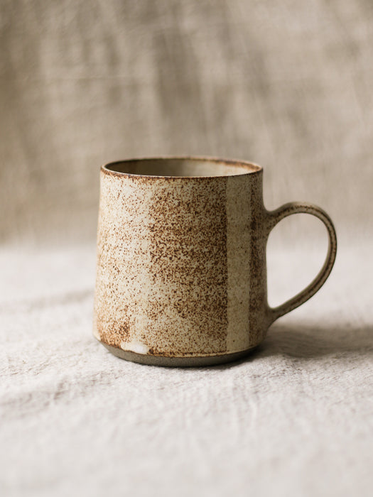 Speckled ceramic mug on a textured surface with a neutral background