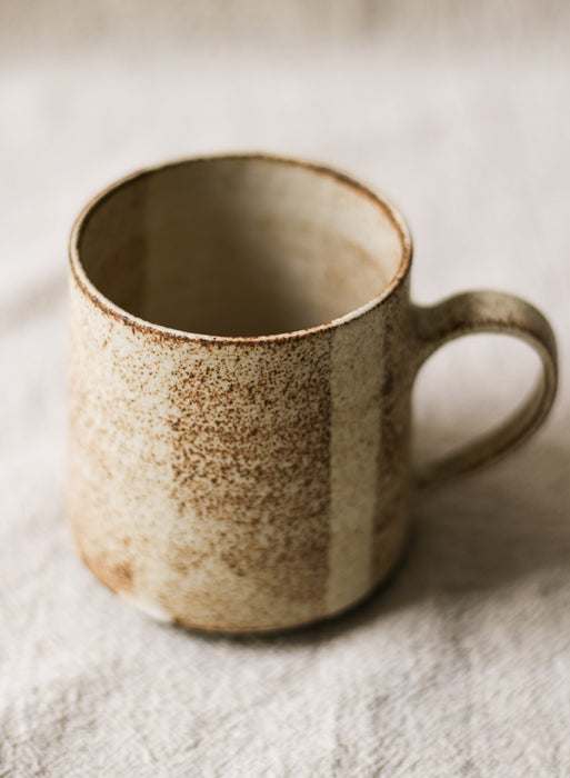 beige speckled ceramic mug on a neutral linen background 