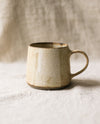 Speckled beige ceramic mug on a textured surface with a neutral background