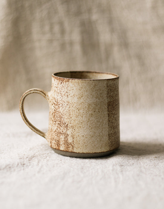 beige speckled ceramic mug with a rustic finish on a neutral background