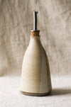 Ceramic oil bottle with metal nozzle on a textured beige background