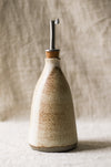 Ceramic oil bottle with cork stopper on a textured surface