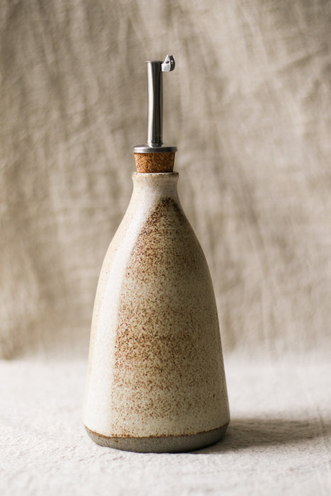 Ceramic oil bottle with cork stopper on a textured surface