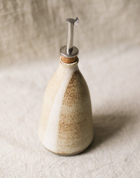 Ceramic oil bottle with a cork lid on a beige background