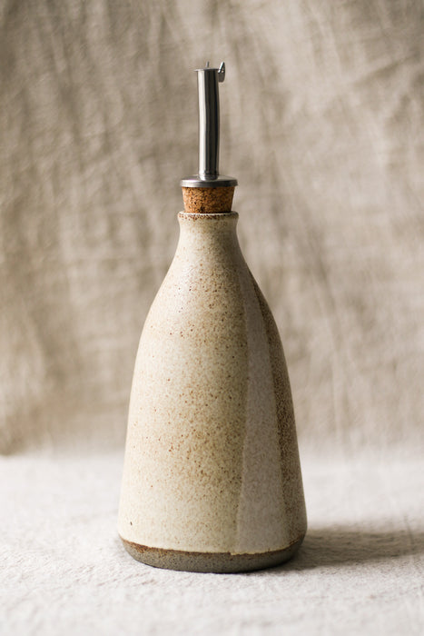 Ceramic oil bottle with metal nozzle on a textured beige background