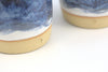 Close-up of two ceramic cups with blue glaze and beige bases on a white background