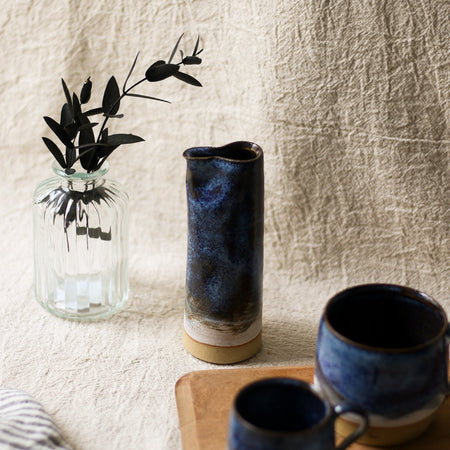 Two blue ceramic mugs and a blue vase on a wooden surface with a textured beige wall background.
