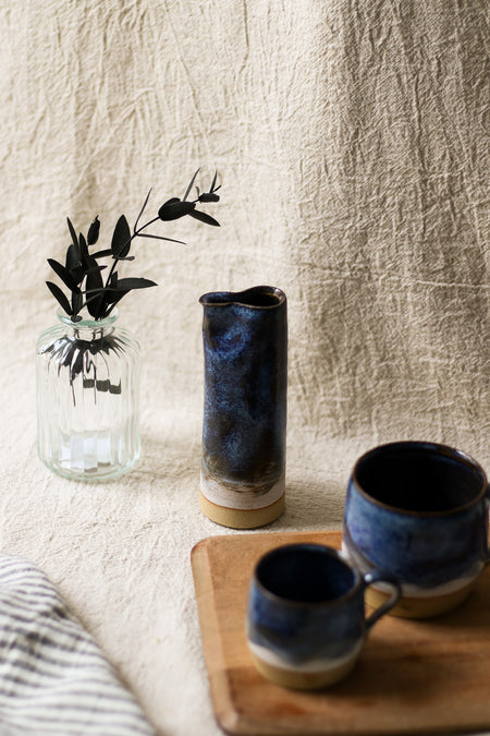 Two blue ceramic mugs and a blue vase on a wooden surface with a textured beige wall background.