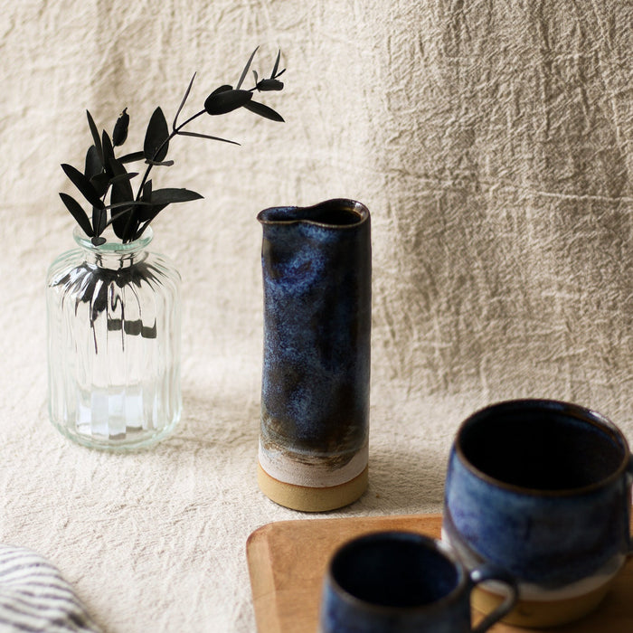 Two blue ceramic mugs and a blue vase on a wooden surface with a textured beige wall background.