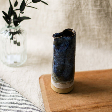 Cylindrical ceramic jug with blue glaze on a wooden surface