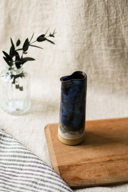 Cylindrical ceramic jug with blue glaze on a wooden surface