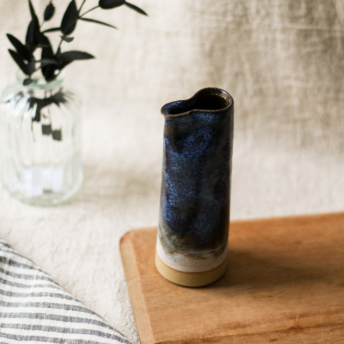 Cylindrical ceramic jug with blue glaze on a wooden surface