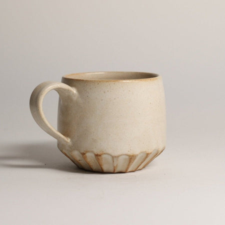 Beige ceramic mug with a carved bottom on a light grey background