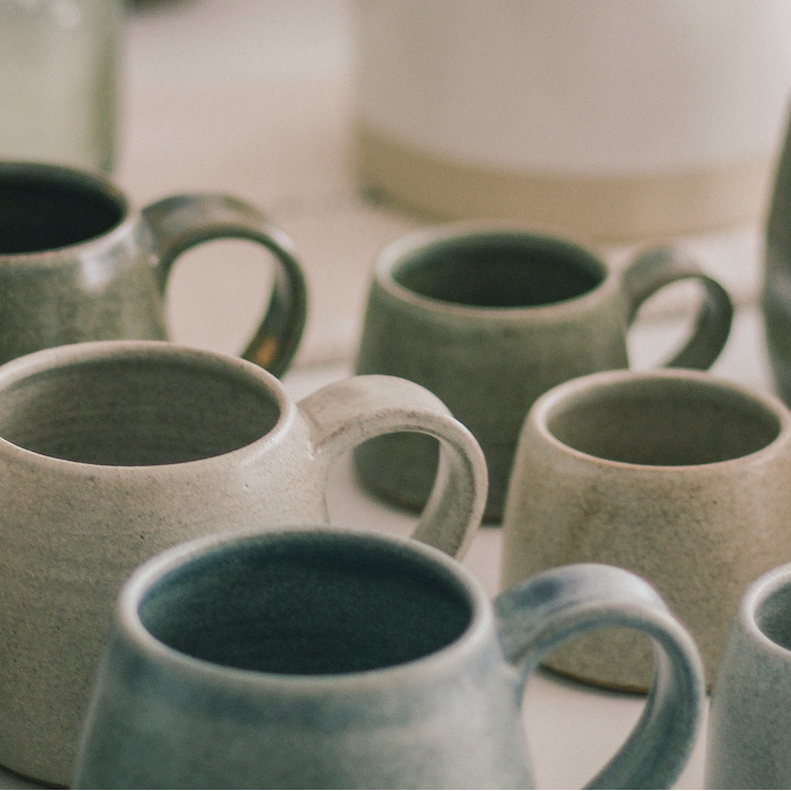 Collection of ceramic mugs in various shades of green and gray on a light surface.
