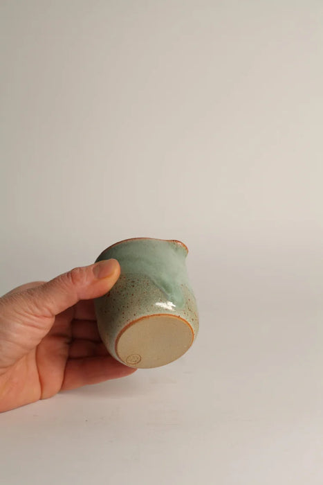 Hand holding a green ceramic jug against a plain grey background