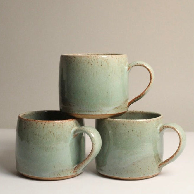 Three green ceramic mugs, stacked, on a light grey background