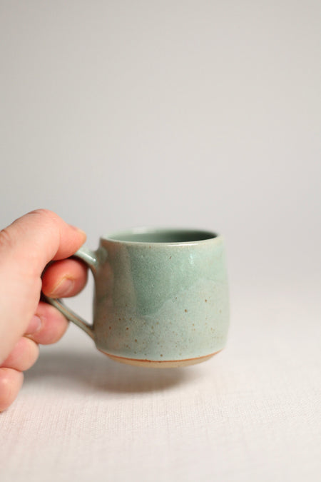 Hand holding a green ceramic mug against a light background