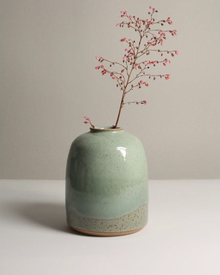 A stoneware ceramic vase with a sea kelp green glaze, displaying a small branch with red berries.