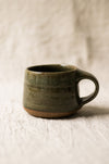 Green ceramic mug on a textured beige surface