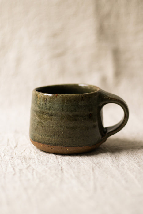 Green ceramic mug on a textured beige surface
