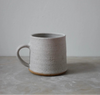 Speckled  white ceramic mug on a grey surface with a light grey background