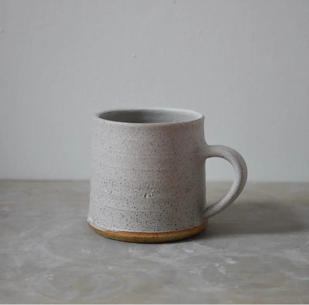 Speckled ceramic mug on a grey surface with a light grey background