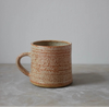 Ceramic mug with speckled brown glaze on a grey surface and background