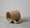 Brown speckled ceramic mug on a grey surface with a grey background