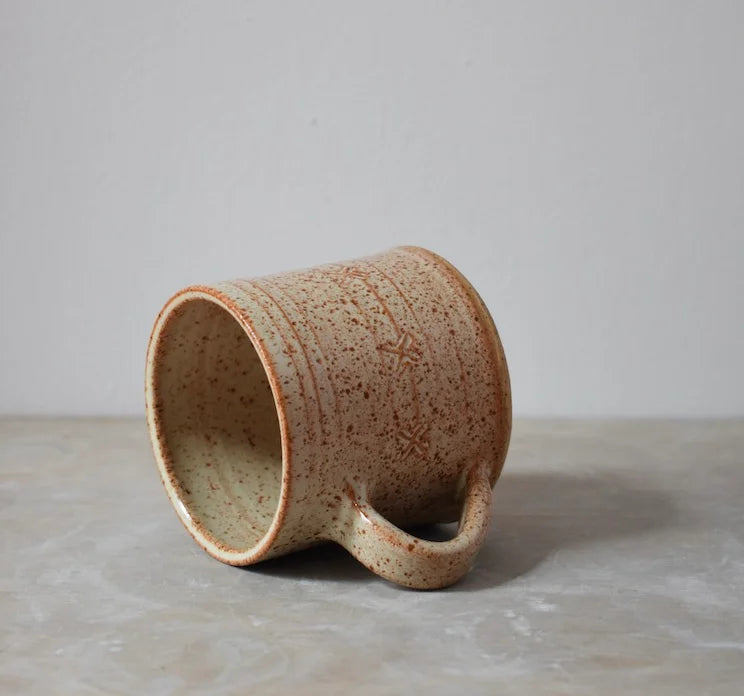 Brown speckled ceramic mug on a grey surface with a grey background