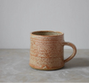 Speckled brown ceramic mug on a grey surface with a light grey background