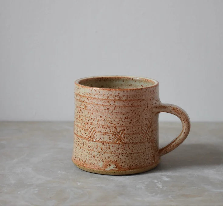 Speckled brown ceramic mug on a grey surface with a light grey background