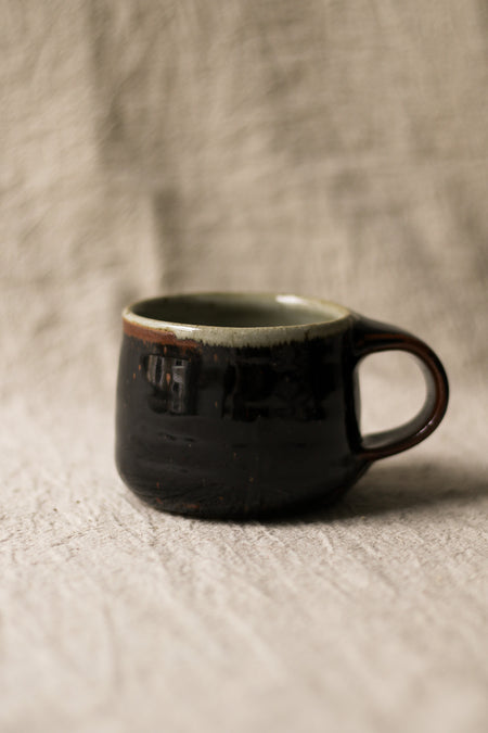 Black ceramic mug on a textured beige surface