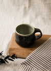 Dark brown ceramic mug on a wooden board with a striped fabric and leaves in the background