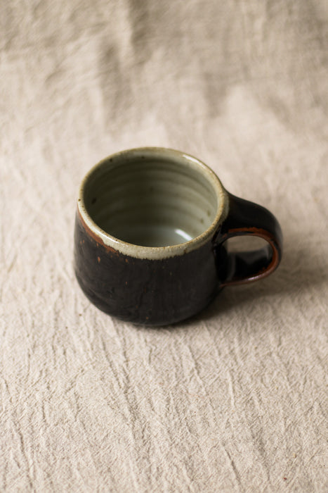 Dark brown ceramic mug on a textured beige surface