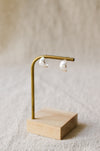 A pair of silver crescent-shaped stud earrings displayed on a brass stand with a light wood base against a soft beige linen background.