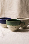 Three ceramic mugs with different color combinations on a textured surface.