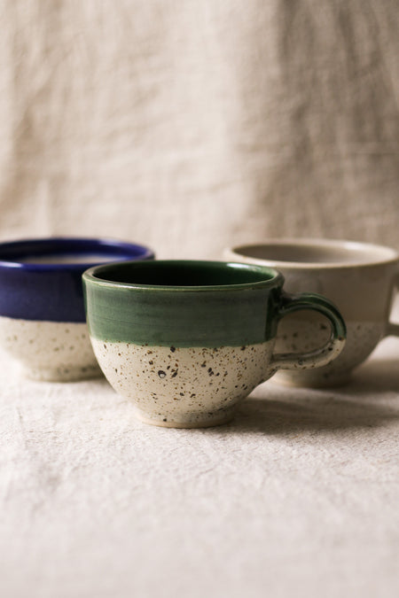 Three ceramic mugs with different color combinations on a textured surface.